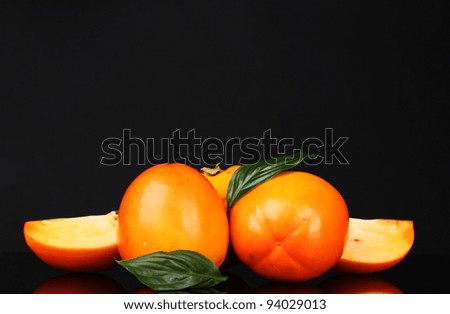 Appetizing persimmons with green leaves isolated on black