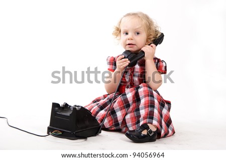 The little curly-haired blonde girl, wearing a checkered dress, talking on the old black phone, calling mom isolated on white. Retro style