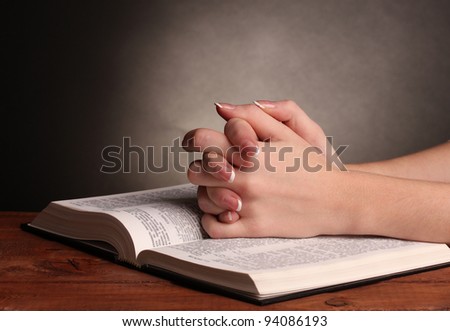 Hands folded in prayer over open russian Holy Bible on black background