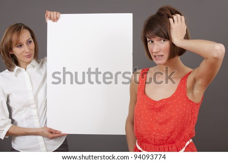 businesswoman holding a blank white board selling or showing something, another woman finds it hard to make a decision.