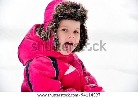 Winter portrait of small girl in pink snowsuit and warm hat catching snowflakes with a tongue