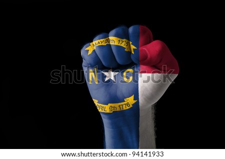 Low key picture of a fist painted in colors of american state flag of north carolina