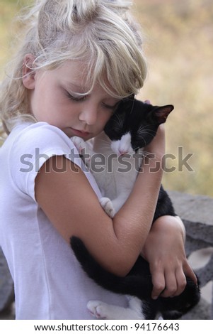 A young girl is sweetly hugging her black and white cat. Both have their eyes closed.
