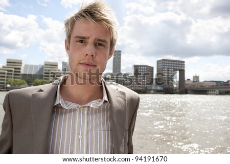 Young businessman standing by river with large city skyline in the background.