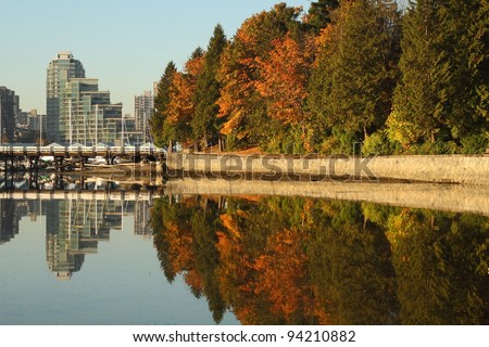 Trees and the pedestrian seawall of Stanley Park reflected in the calm waters of Coal Harbor. Vancouver, British Columbia, Canada.