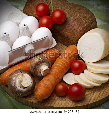 Still life from vegetables, eggs and bread on wooden placemat