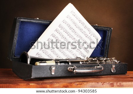 old clarinet and notebook with notes in case on wooden table on brown background