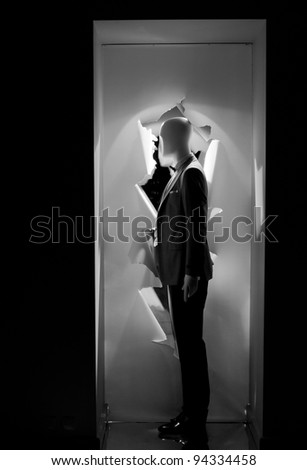 a male mannequin dressed the highlighted in a shop window decorated by torn like paper in grayscale Royalty-Free Stock Photo #94334458