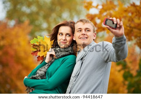 Two Smiling young people taking a picture with mobile phone in autumn park outdoors