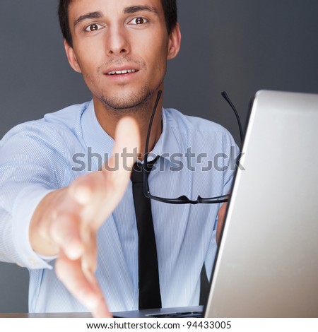 Businessman gives a handshake. Sitting near his laptop at his desk