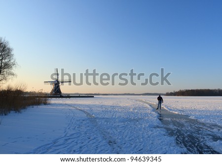 Ice skater on a frozen lake and near a traditional windmill in Holland.