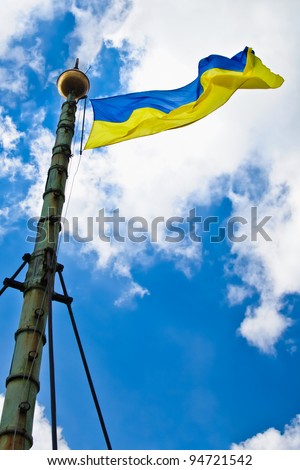 Flag of Ukraine with flag pole waving in the wind on front of blue sky with clouds