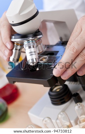 A medical or scientific researcher using a microscope in a laboratory environment with test tubes and laboratory equipment