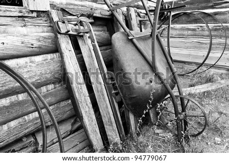 Old steel wheeled wheelbarrow leaning against old log building.