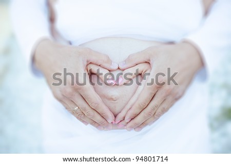 happy young couple standing on the shore of the lake hugging. Closeup pictures of pregnant girls belly with his hands folded in heart
