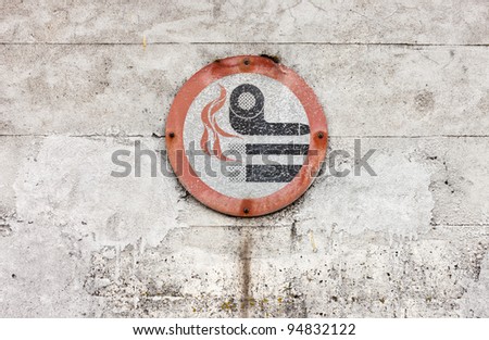 Weathered No Smoking sign against a concrete wall.