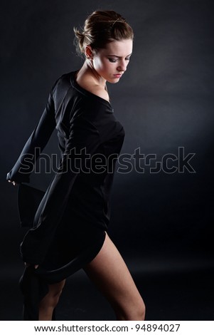 A beautiful brunette girl posing in a studio wearing a black dress.