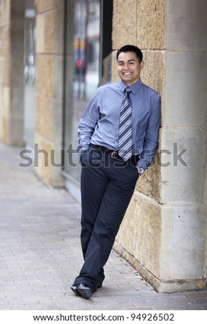 Stock photo of a Hispanic businessman leaning against a stone wall in a business district.