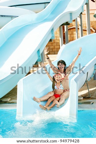 Child with mother on water slide at aquapark. Summer holiday.