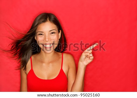 woman showing pointing on red background. Very fresh and energetic beautiful young multiracial Chinese Asian / Caucasian girl smiling happy presenting on red background.