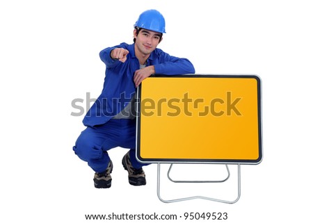 Man kneeling by road sign and pointing