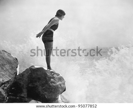 Female swimmer on rock above crashing surf Royalty-Free Stock Photo #95077852