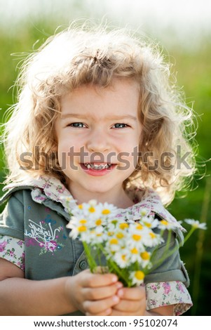 Happy smiling child with bunch of spring flowers in field