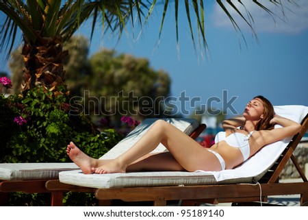 Beautiful girl lying on a deckchair and tanning