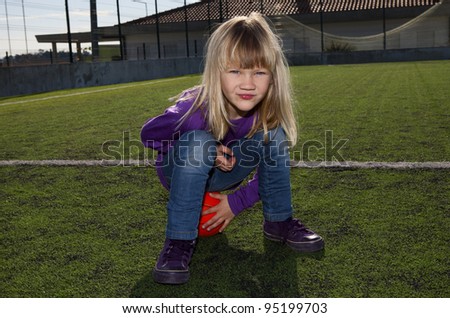 Little girl sitting on a basketball on an outdoor court