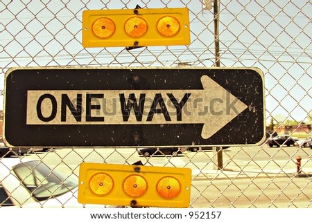 One-way street sign on chain link fence in inner city.