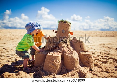 Two little boys building large sandcastle on the beach Royalty-Free Stock Photo #95374099