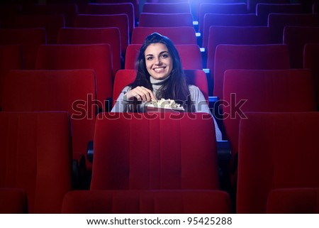 portrait of a pretty young woman, she sitting in an empty theater, eats popcorn and smiles