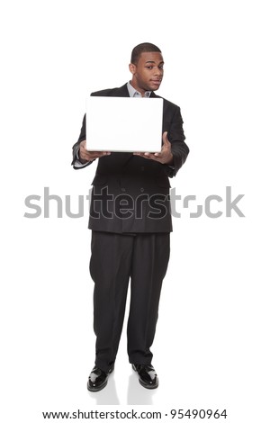 Isolated studio shot of an African American businessman standing and looking warily at a laptop comptuer he is holding out in his hands.