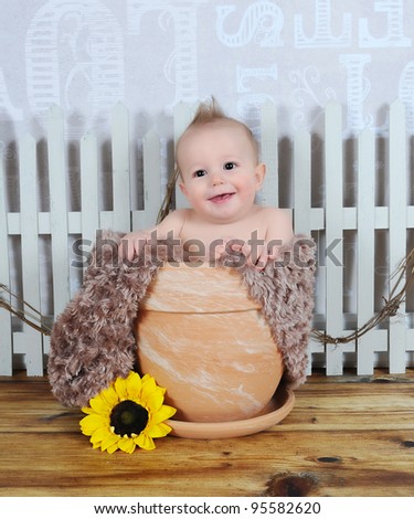 adorable and happy baby boy sitting in clay flower pot