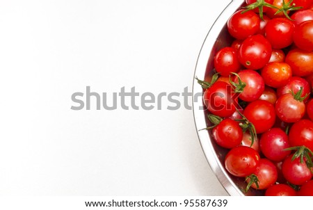 A stock photo of a stainless steel colander of fresh cherry tomatoes sitting on a textured kitchen counter top