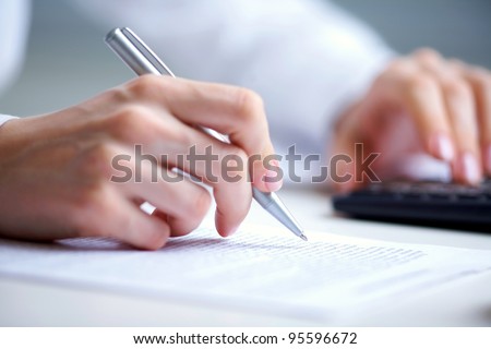 Photo of hands holding pen under document  and pressing calculator buttons