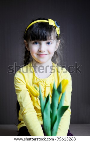 Portrait of a sunny child girl with bouquet of yellow tulips on a dark background