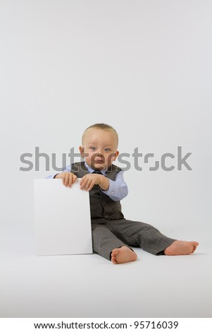 Photograph of a baby dressed smartly in business clothing whilst holding a blank piece of card, shot against white.