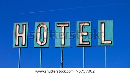 Grungy old hotel sign isolated on a blue sky background with an airplane flying in the distance