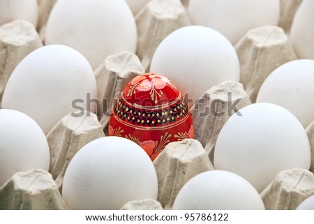 Painted Easter egg among white fresh eggs in carton packaging