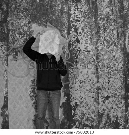 Man with piece of torn wallpaper in decayed room. Black and white.