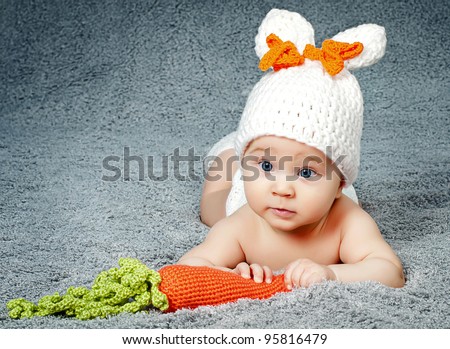 A small child with a rabbit ears. Lying on his stomach with a carrot.