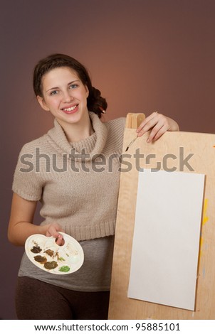 Girl teenager standing near easel with palette and brush