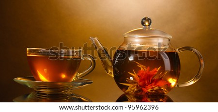 glass teapot and cup with exotic green tea on wooden table on brown background