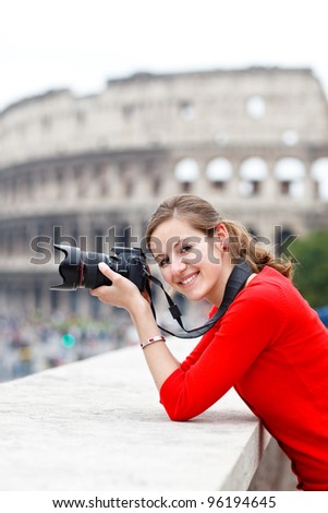 Portrait of a pretty young tourist taking photographs while sightseeing in Rome, Italy (with Colosseum in the background)