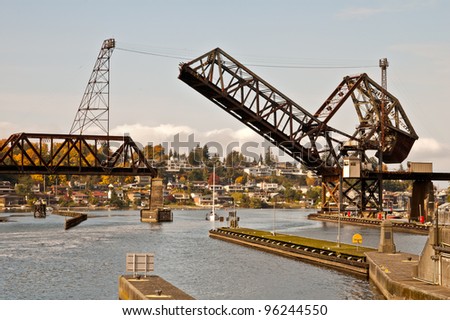 A railroad bridge raises to allow a sailboat room to pass underneath on a waterway in the Seattle, Washington area.