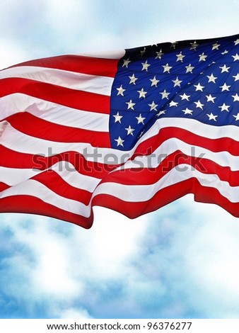 United States flag flying against a cloudy blue sky.