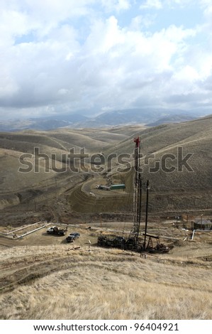 An oil well servicing rig sets up in mountainous country on a California lease