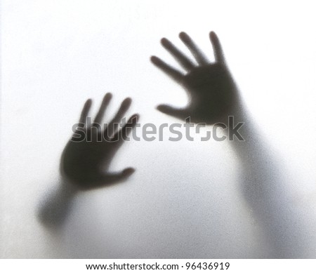 Shadow of  hands for help behind frosted glass in the back light.