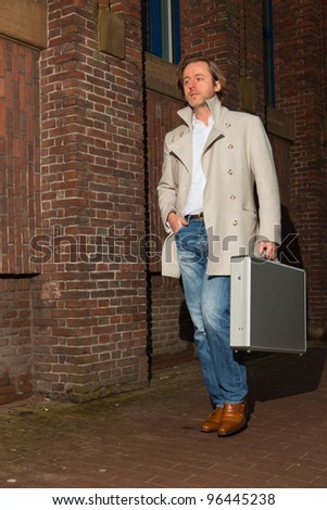 Business man holding briefcase walking on the street. Long hair wearing white coat and jeans.